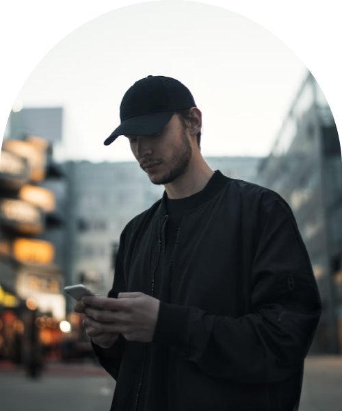Ung man i svart keps och jacka tittar på sin telefon i en stadsmiljö