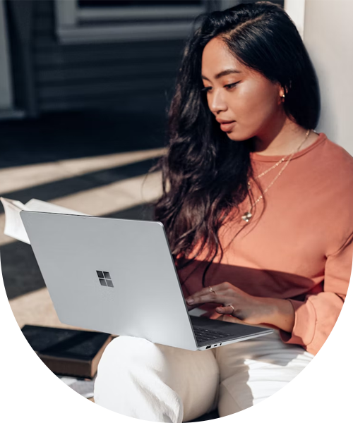 Kvinna håller i en öppen laptop, solljuset skiner på henne